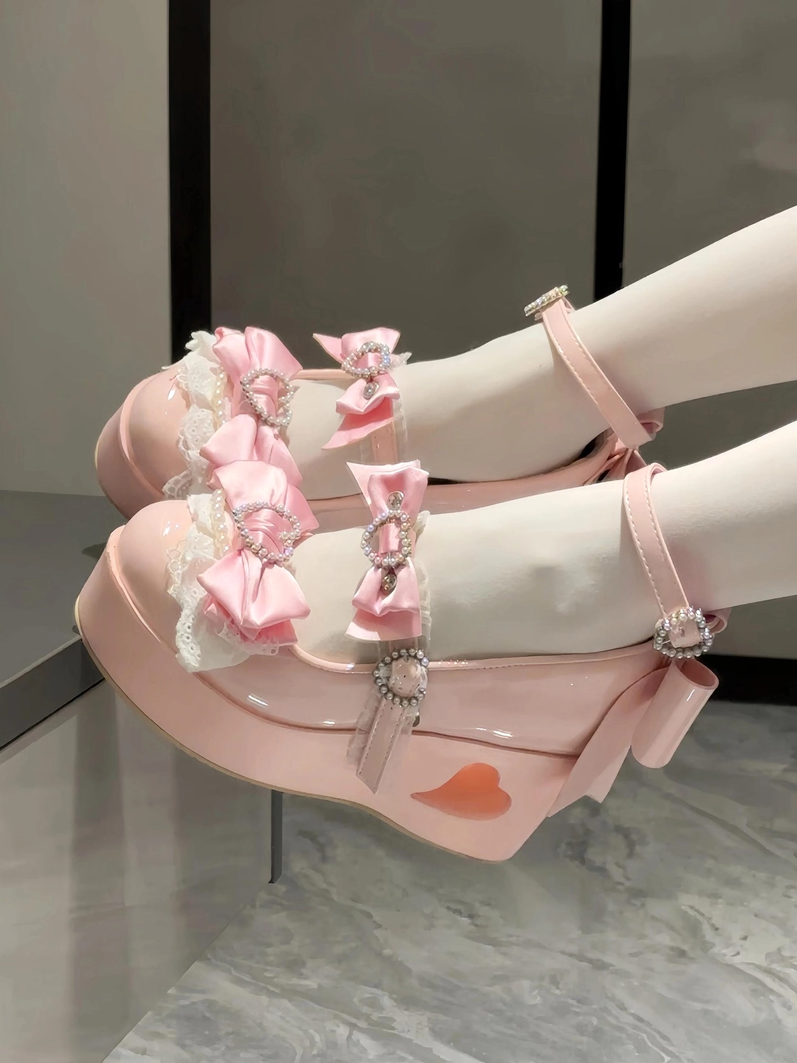 Pink Jirai Kei platform Mary Jane shoes styled on model feet wearing white lace ruffled socks with heart-shaped rhinestone buckles and satin bow trim