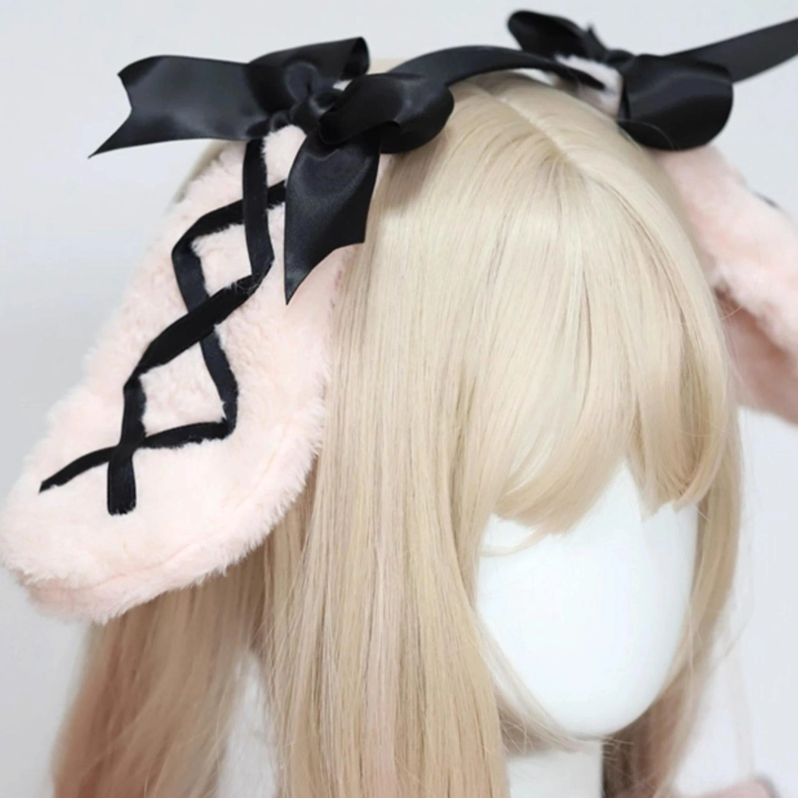 Pink rabbit ear hairband three-quarter side view on mannequin head with fluffy pink ears black crisscross ribbon and black satin bows
