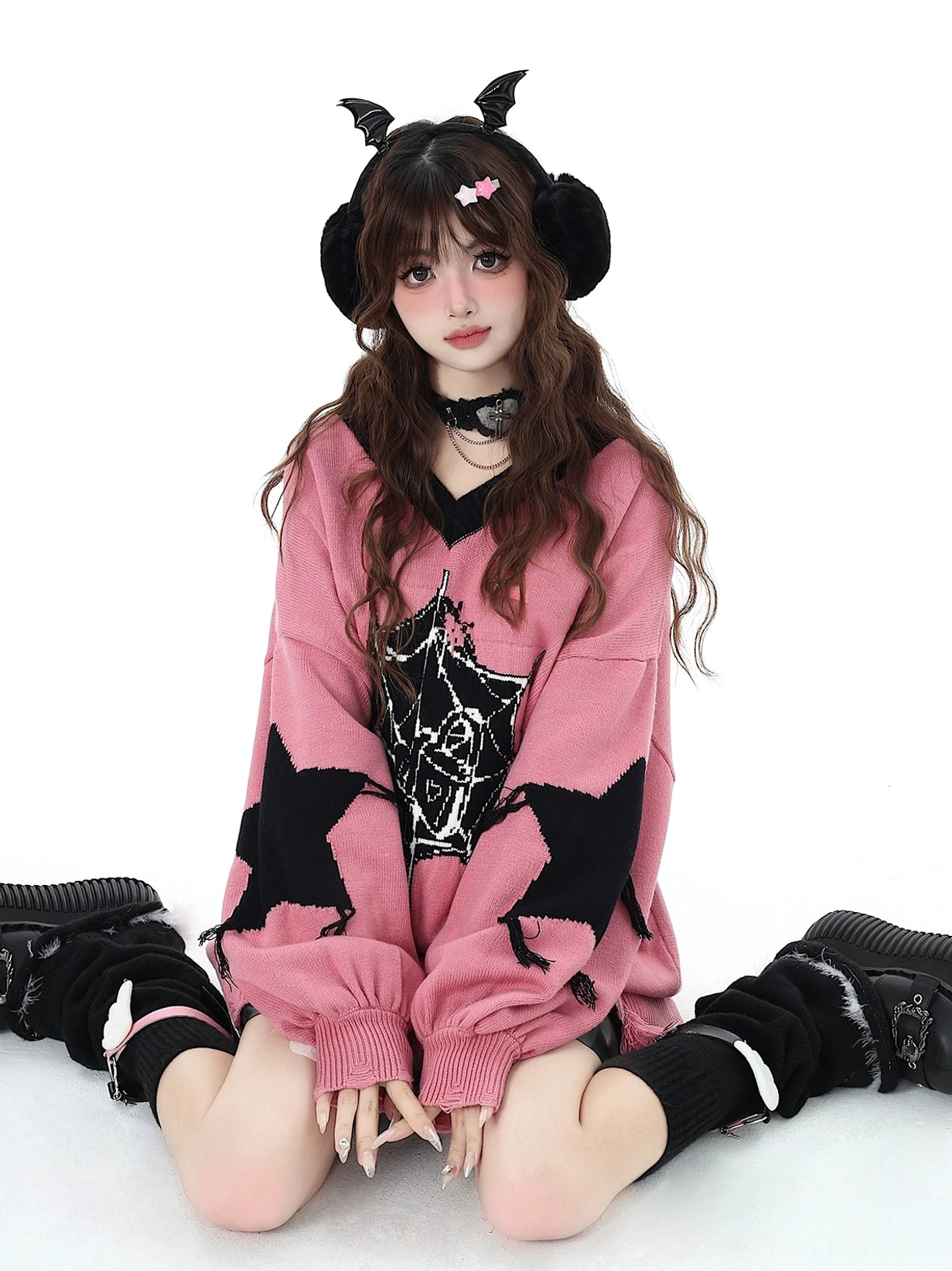 Pink Jirai Kei knit sweater with distressed side detail worn by model with devil horn earmuffs in sitting position with hands on knees