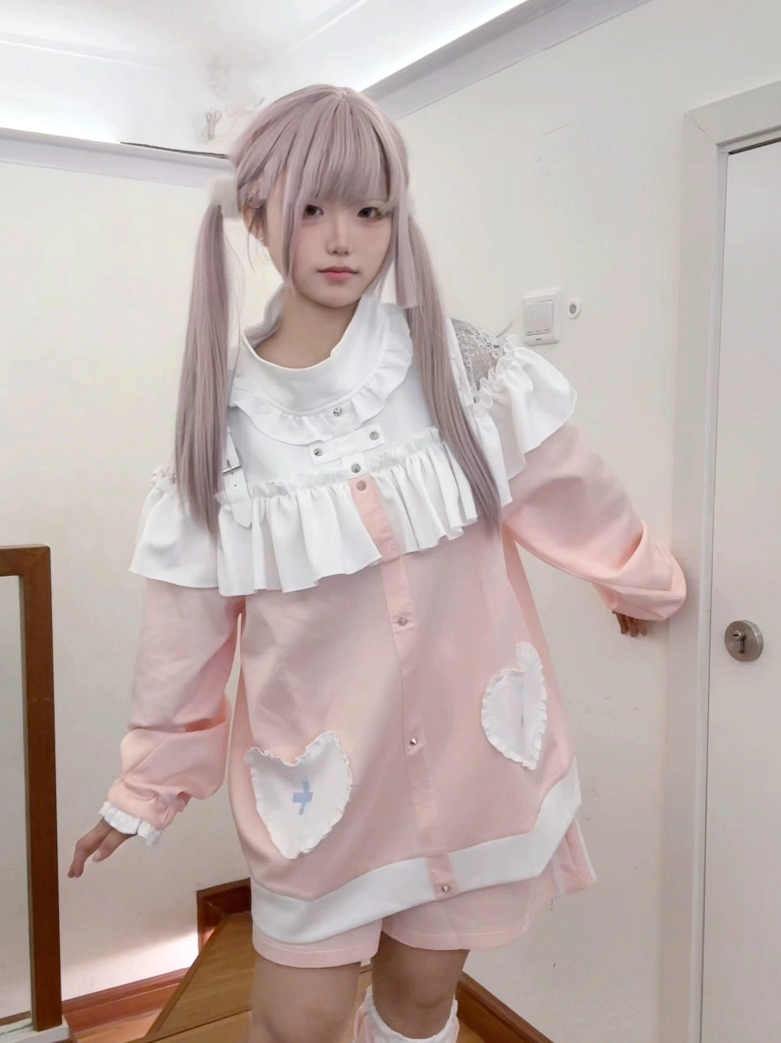 Pink sweatshirt and shorts set side shot with hand resting on door, showing heart-cross patches, white ruffled collar and loose fit silhouette