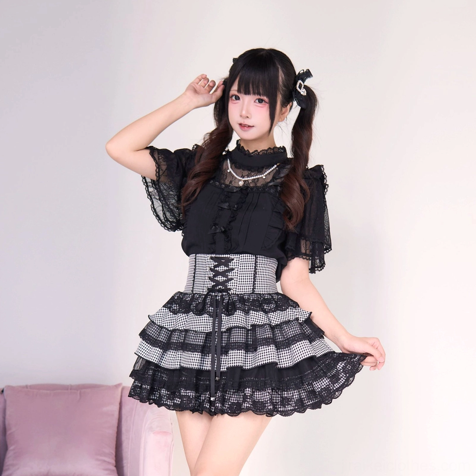 Black and gingham plaid jirai kei tiered cake skirt with gothic lolita blouse, three-quarter front angle displaying pearl necklace corset waistband checkered layered skirt and lace hem