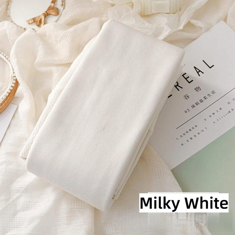 Plain milky white solid footed tights folded on warm home textile background, flat lay shot displaying smooth plain knit fabric and creamy white tone ideal for clean Jirai Kei aesthetic foundation layering
