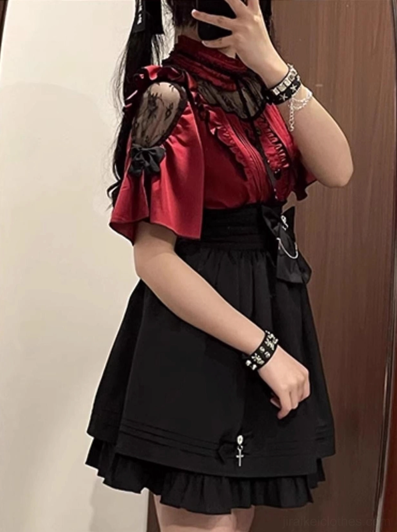 Side half-body mirror selfie of female model wearing cold-shoulder red ruffled lace blouse with high-waist black skirt and rhinestone cross pendant accessory