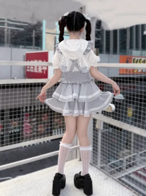 Back view of ryousangata sweet lolita two-piece outfit showing hooded collar smocked waist ruffled mini skirt and lace knee socks on female model with twin tails