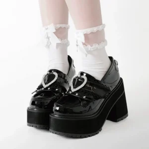 Black patent leather heart buckle platform loafers close-up front view of feet showing pearl-embellished heart strap, glossy upper, and chunky block heel with model wearing frilled bow white ankle socks