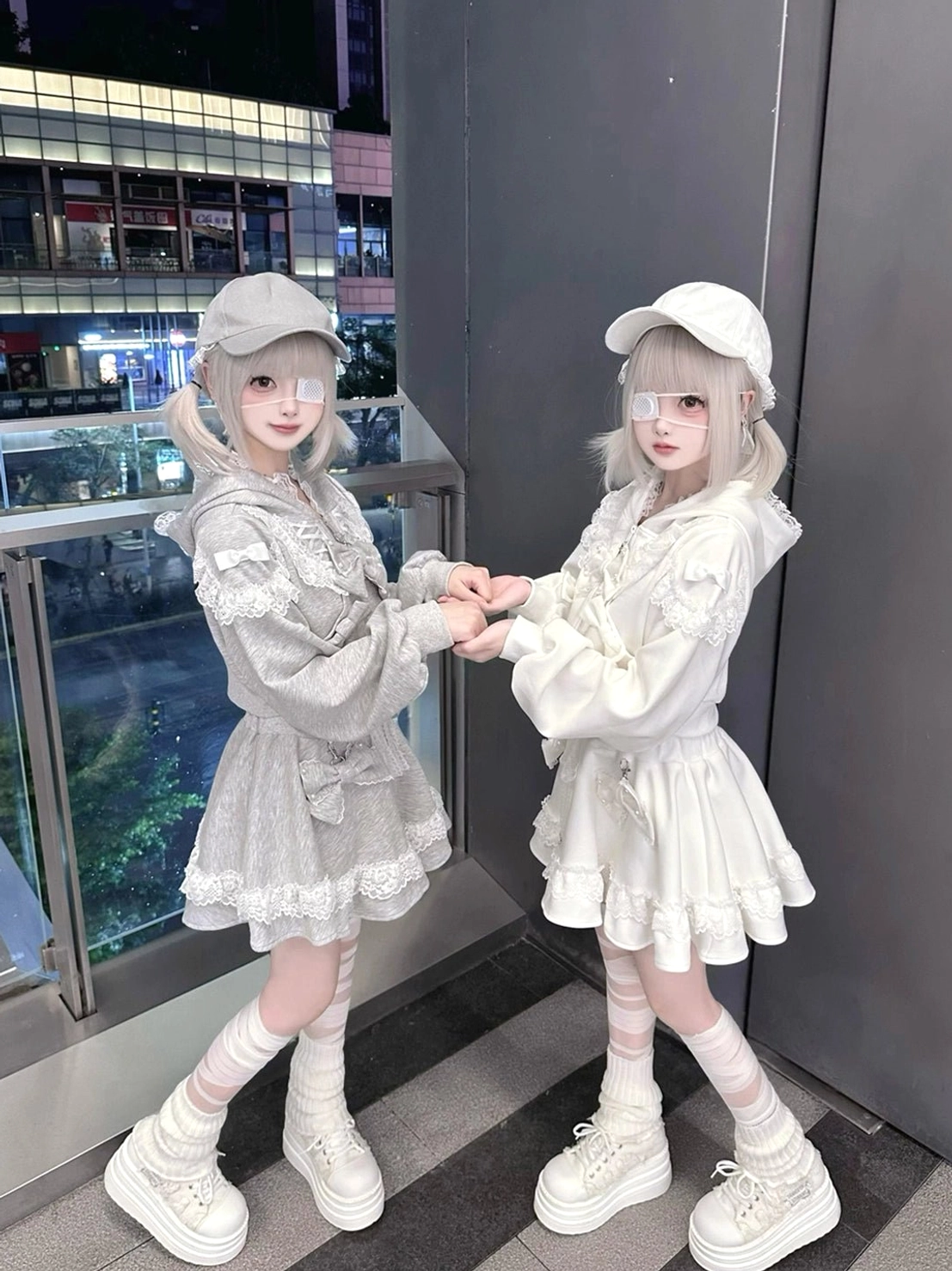 Side pose of twin models in ryousangata lace sets, white platform shoes and twin ponytails, mall balcony railing
