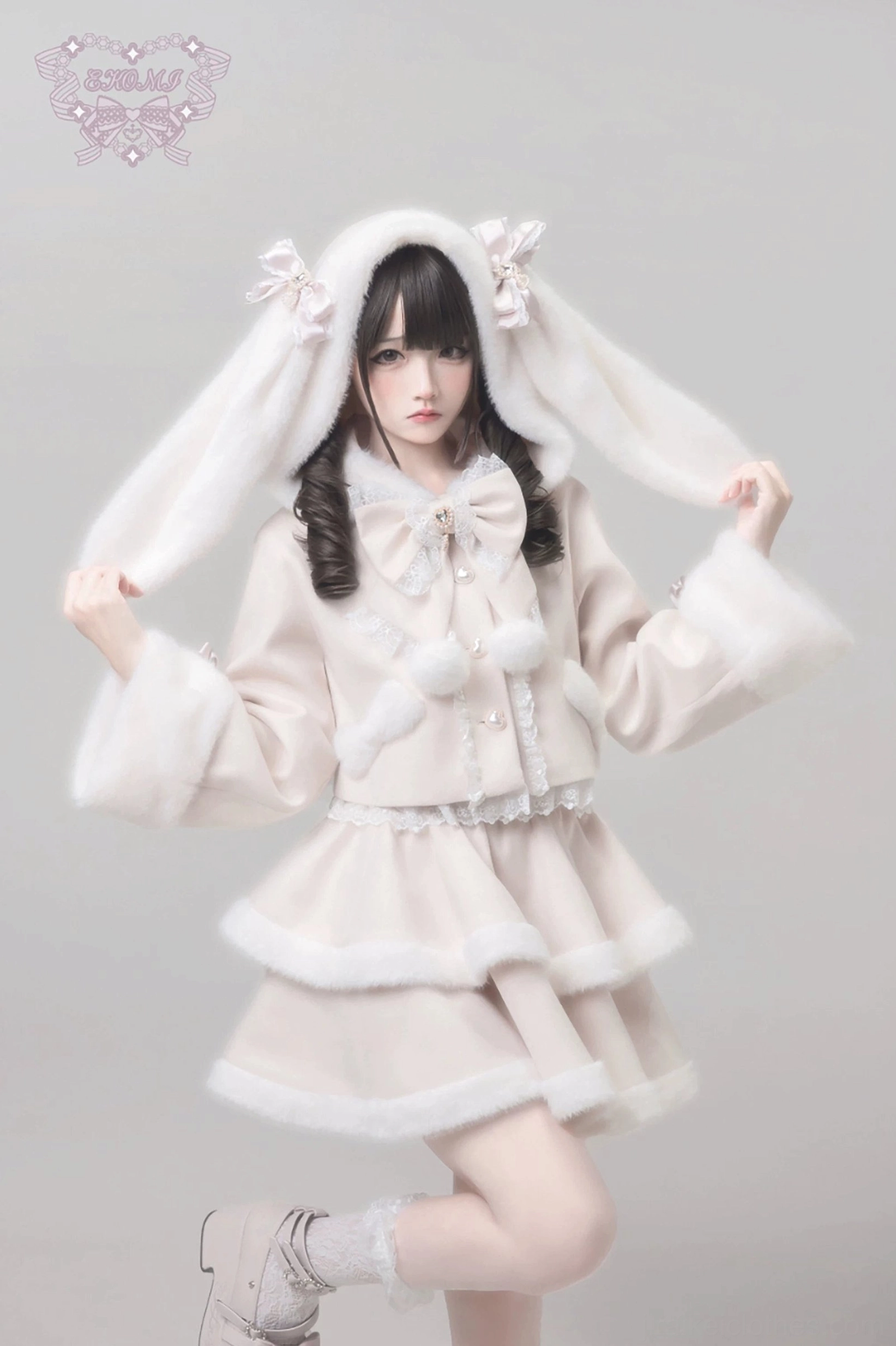 Ryousangata winter coat with detachable bunny ear hood and tiered ruffle skirt in beige, Jirai Kei lolita outfit with fluffy fur trim and heart-shaped buttons, three-quarter view squatting pose