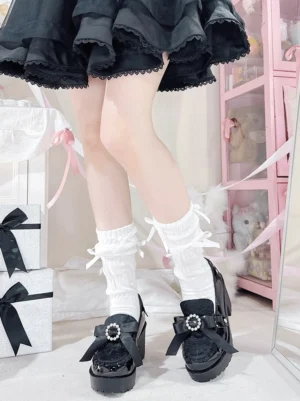 Ryousangata platform Mary Jane heels with rhinestone bow buckle and ribbon details, shown on legs wearing frilly white socks and black ruffled skirt, front low angle view