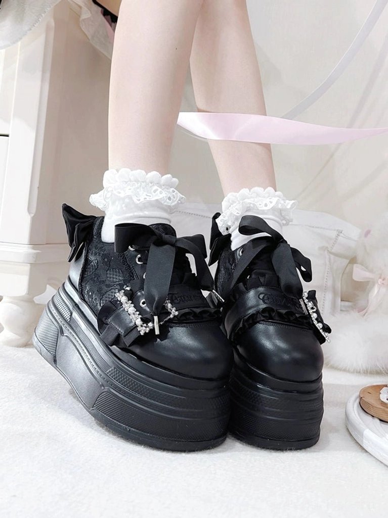 Black Jirai Kei platform shoes front view on feet with frilly white sock cuffs, showing satin back bow, rhinestone buckle strap and extra thick platform