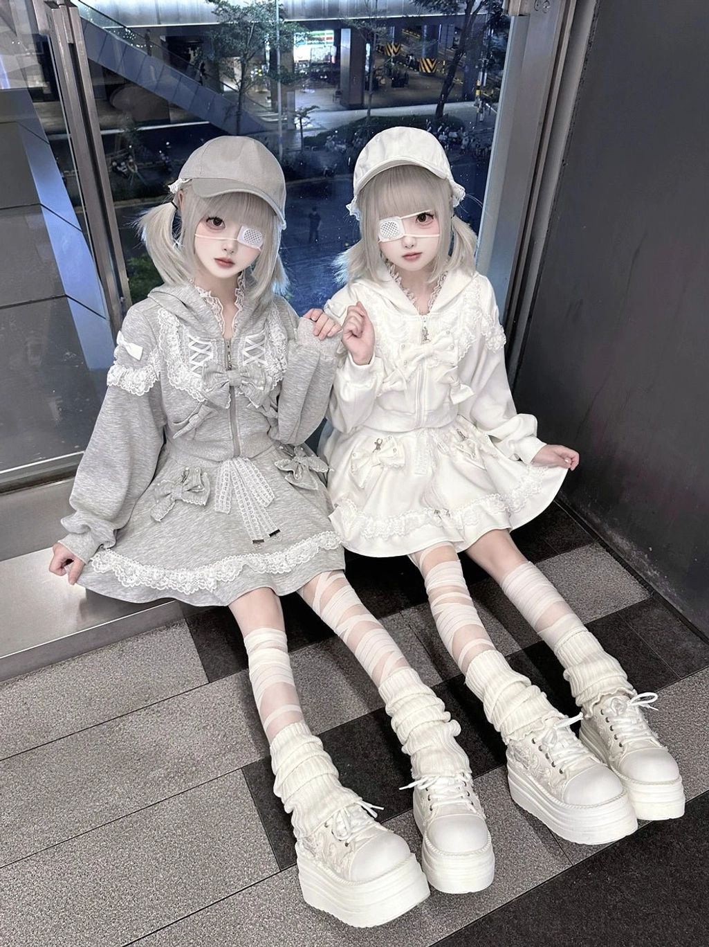 Sitting pose of twin models wearing relaxed ryousangata lace hoodies and skirts, street lolita fashion mall floor scene