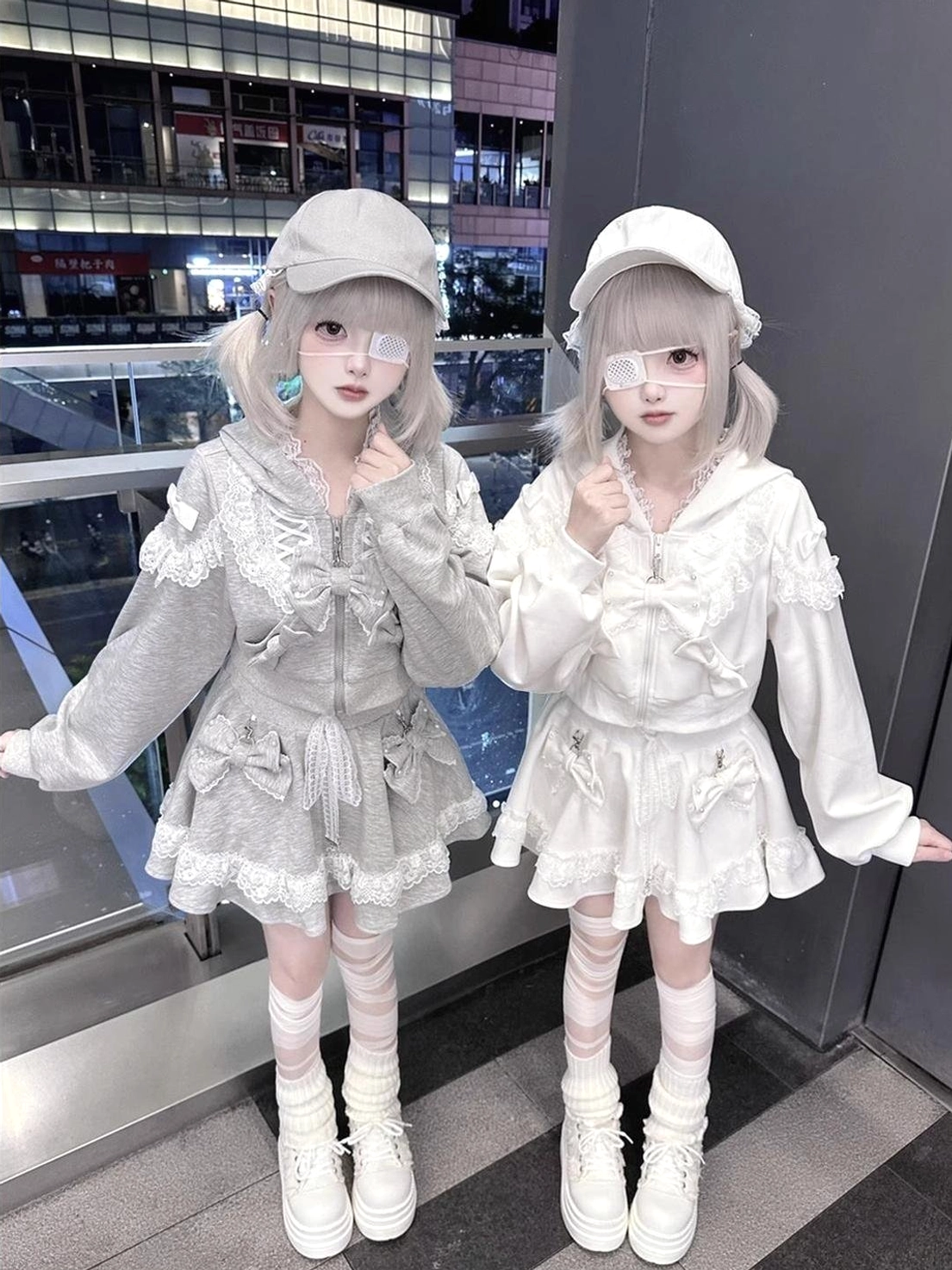 Twin models wearing gray and white ryousangata lace zip hoodies with pleated skirts, jirai kei street fashion outdoor mall setting