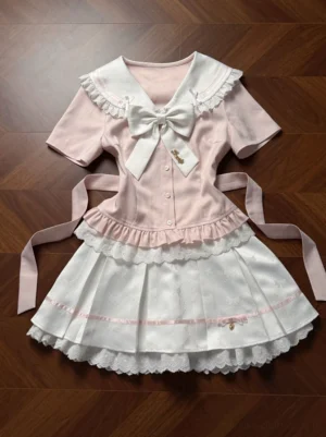 Ryousangata sailor collar lolita blouse and pleated skirt two-piece set in pink and white, flat lay top-down view showing full ensemble with detachable bow tie and double-layered skirt hem on wooden floor background