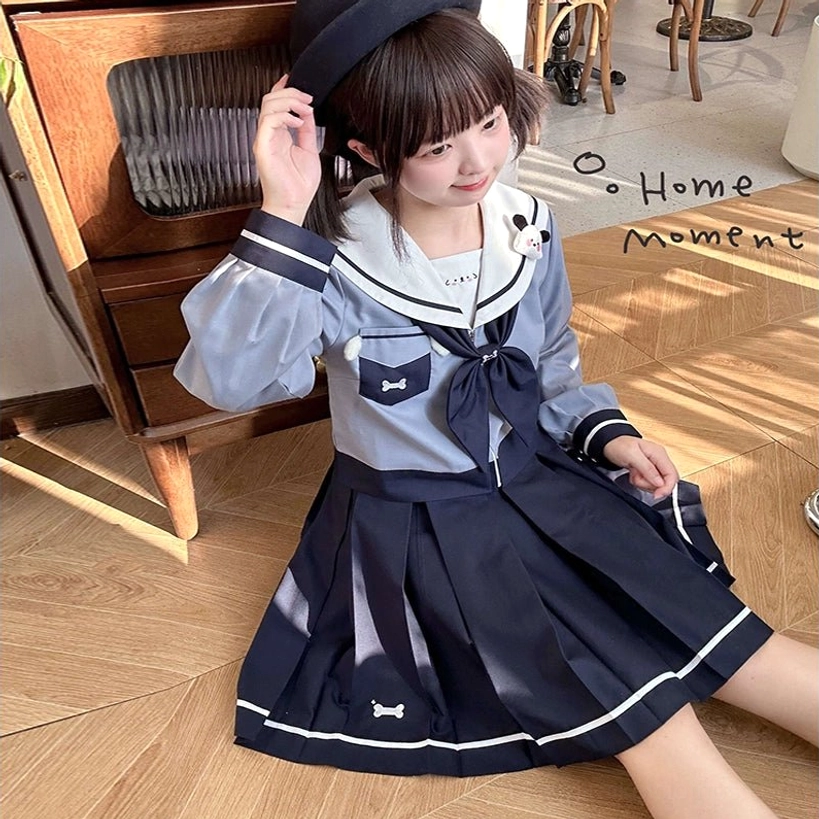 Sailor JK uniform front three-quarter seated angle showing cuffed sleeve detail navy coordinating bow tie pocket bone embroidery home-style indoor backdrop