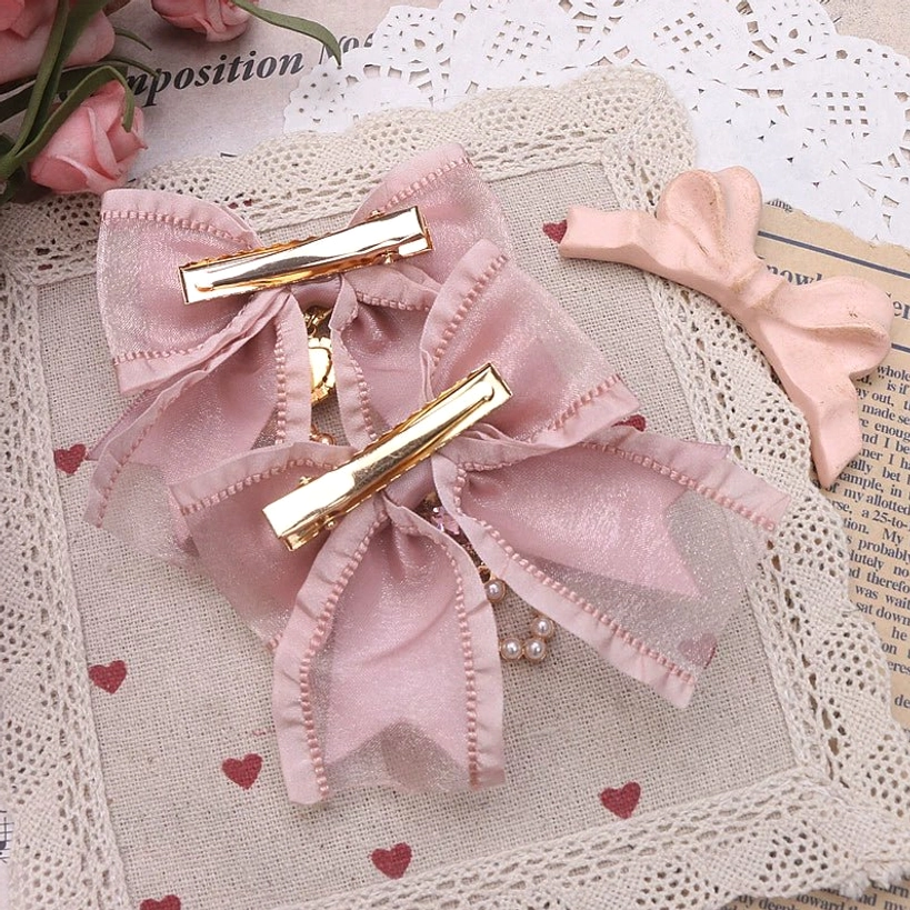 Sheer dusty pink bows with gold alligator clips and pearl chain charms displayed on heart-patterned lace fabric