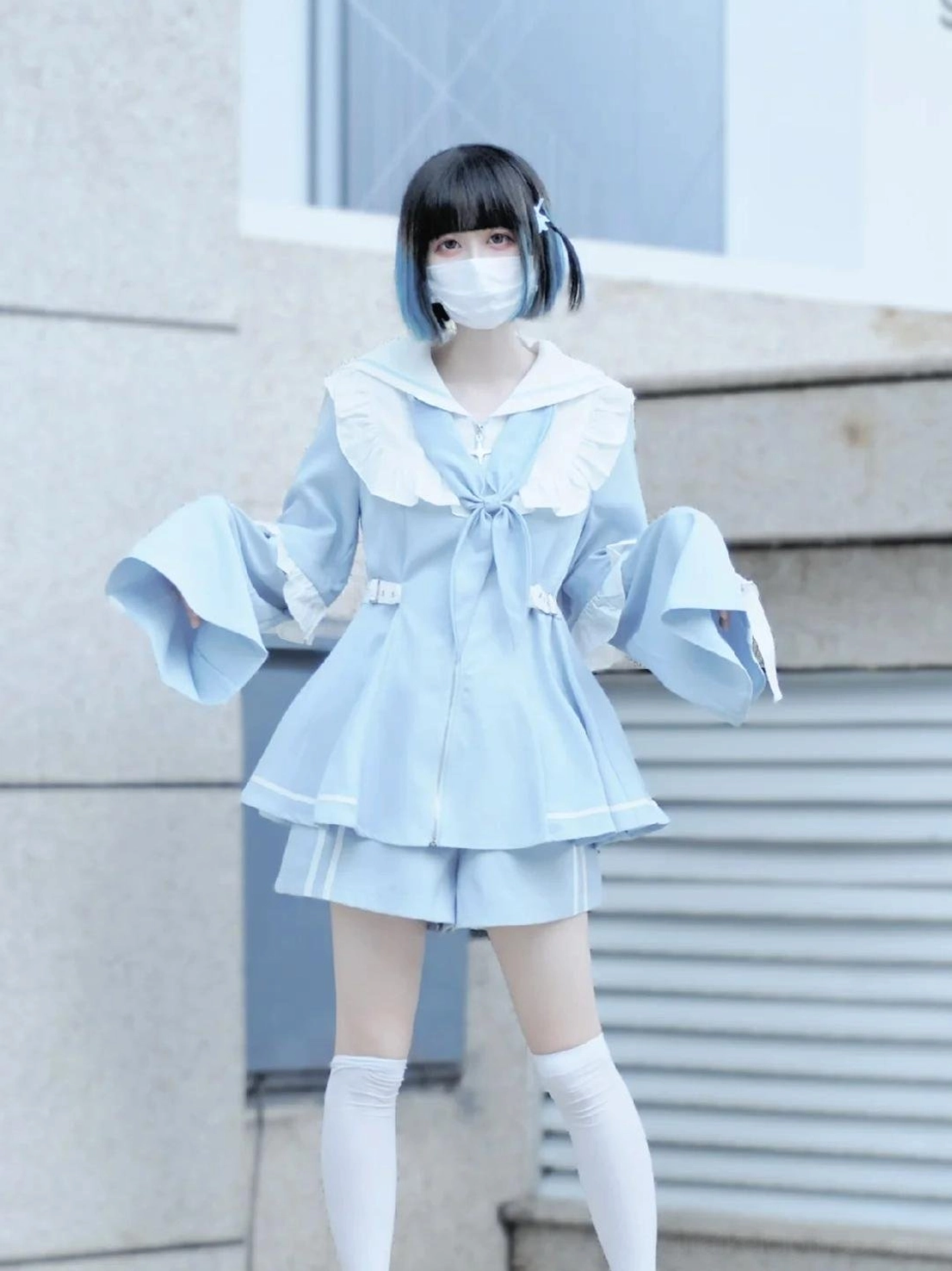Full-body front shot of short-style pastel blue sailor Jirai Kei set with wide flared sleeves, white sailor trim, and matching mini shorts worn outdoors in building corridor setting