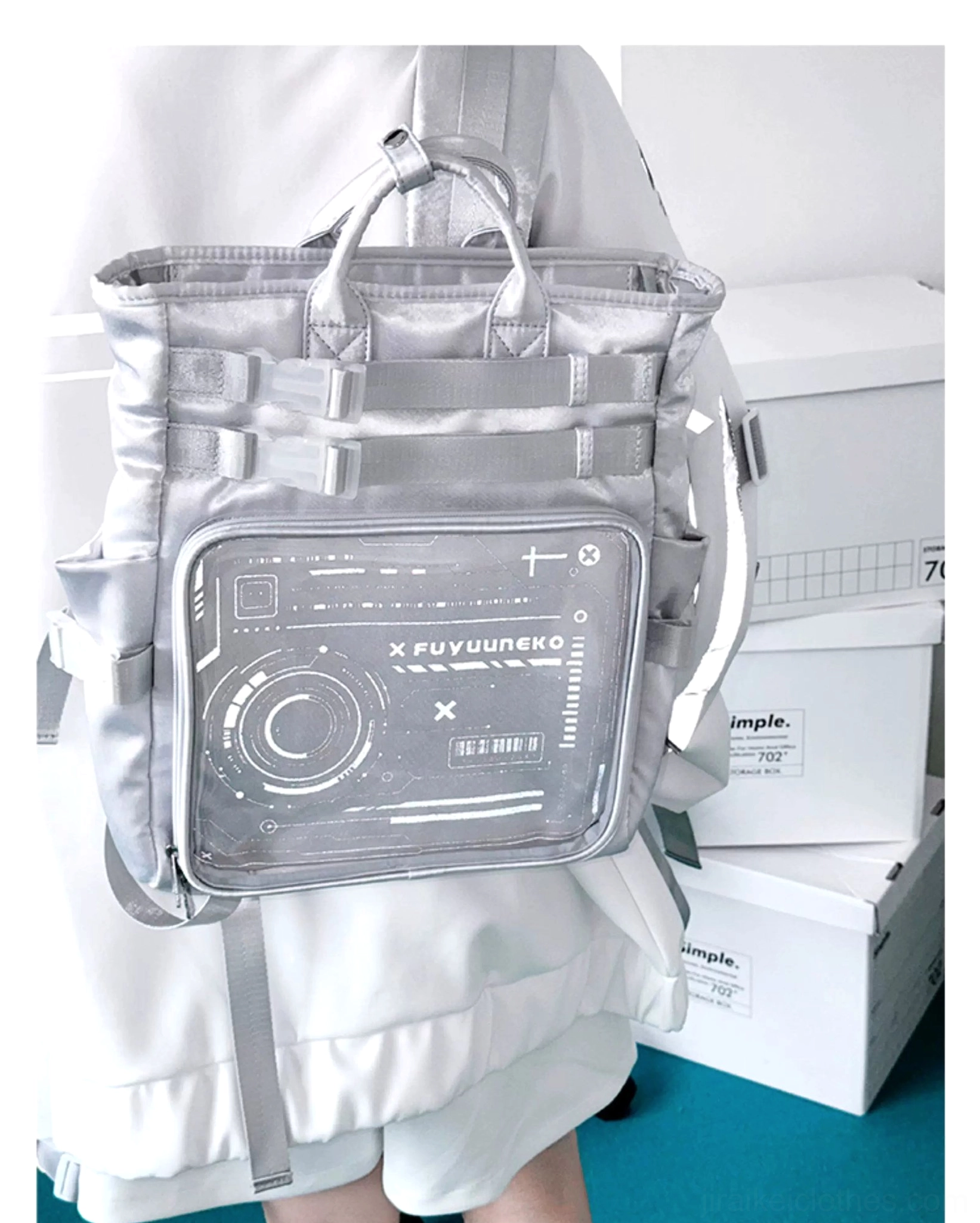 Silver cyberpunk Jirai Kei ita backpack worn on person showing back three-quarter view with clear anime badge display window and top carry handles on office background