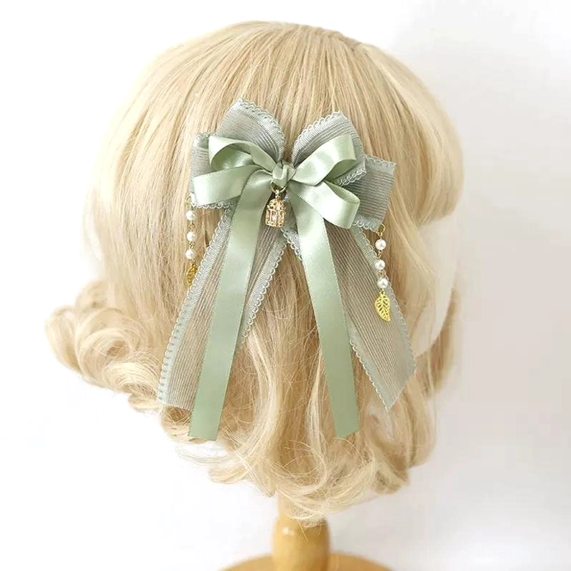 Solid matcha green satin bow hair clip with small gold charm pendants and delicate metalwork details on blonde wig mannequin back view—minimalist Jirai Kei aesthetic hair piece