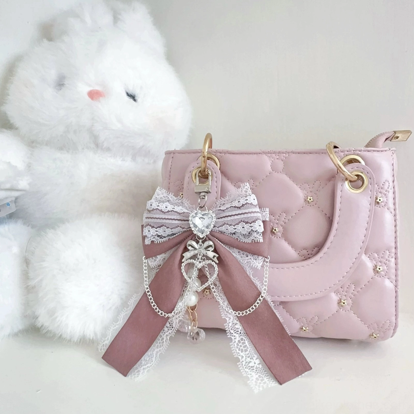 Taupe lace Ryousangata bow bag pendant attached to quilted handbag - close-up detail of heart rhinestone and pearl accents with layered ribbon bow construction