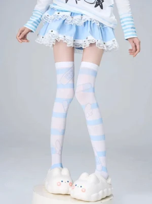 Over-the-knee velvet socks featuring light blue striped pattern with bandage and bear prints, three-quarter front leg perspective, styled with sweet lolita outfit and bunny platform slippers