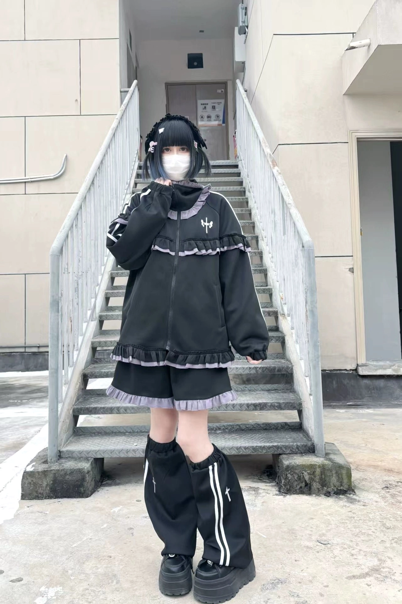 Black-purple ruffle Tenshi Kaiwai tracksuit with wide-leg shorts, striped leg warmers and platform shoes photographed on outdoor stairway