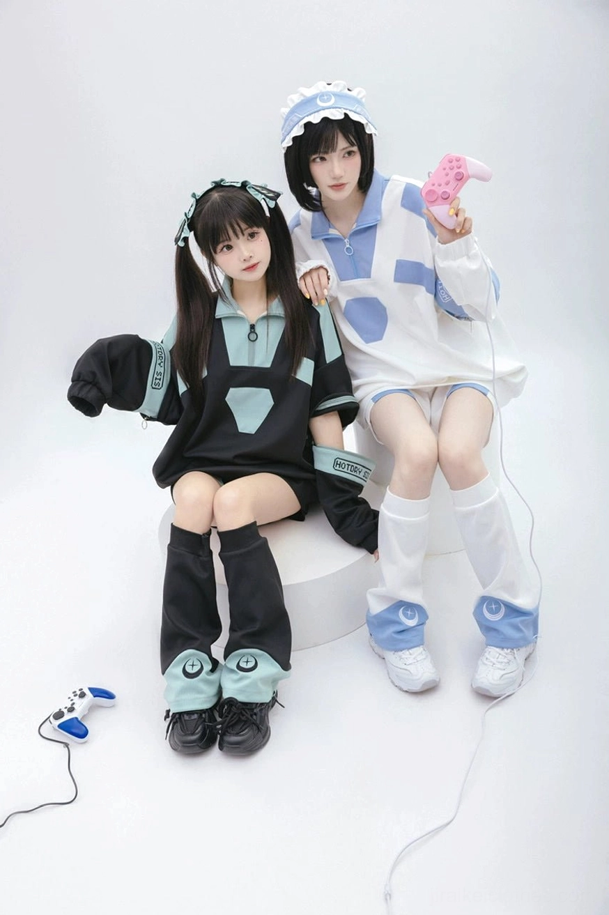 Half-body sitting view of black and teal Tenshi Kaiwai sweatshirt with removable sleeves, model wearing dinosaur bucket hat with pink gaming prop