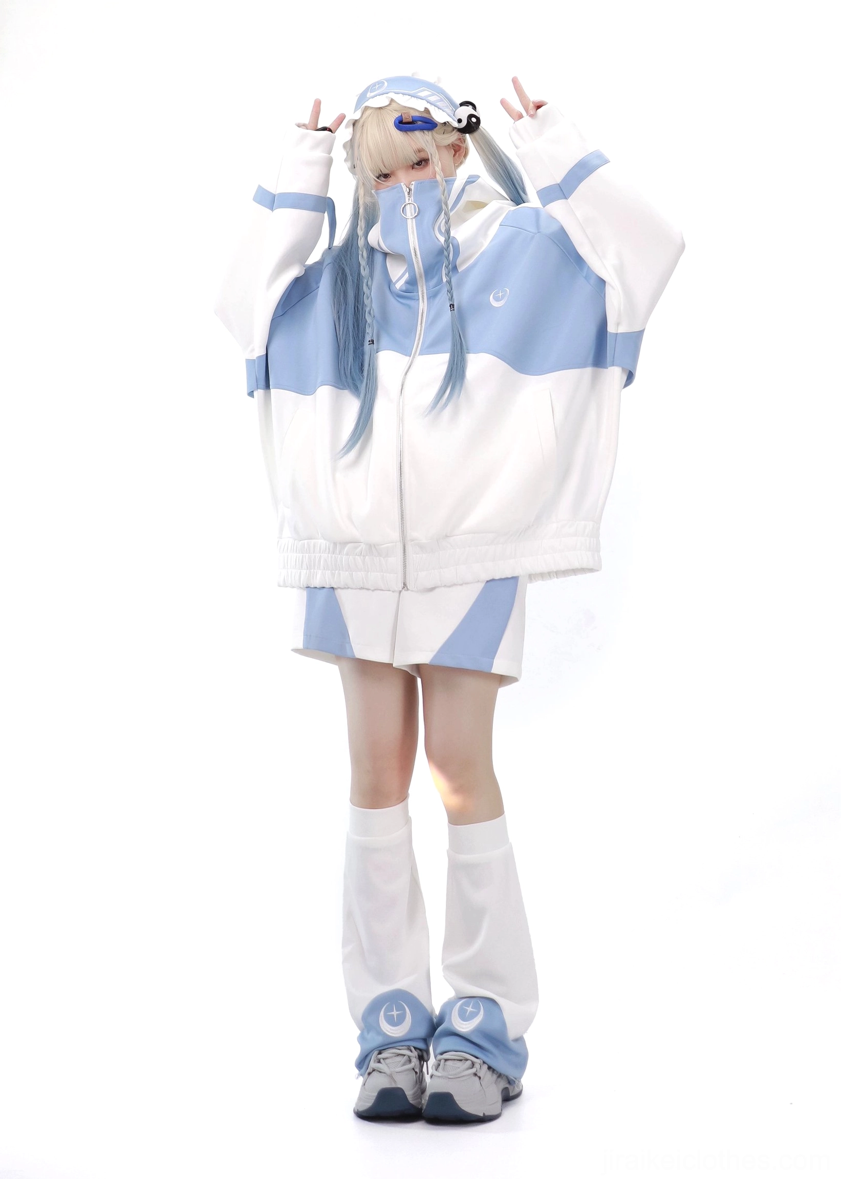 Tenshi Kaiwai blue-white color-block sports suit featuring oversized zip hoodie and matching shorts with long crescent leg warmers on blonde model with raised hands front view