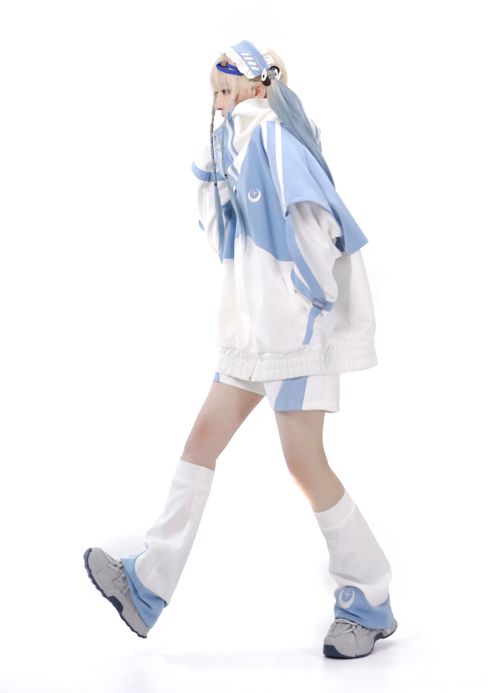 Blue-white Tenshi Kaiwai color-block sports set shown in side profile on blonde female model in walking pose wearing cropped hoodie with crescent leg warmers white studio