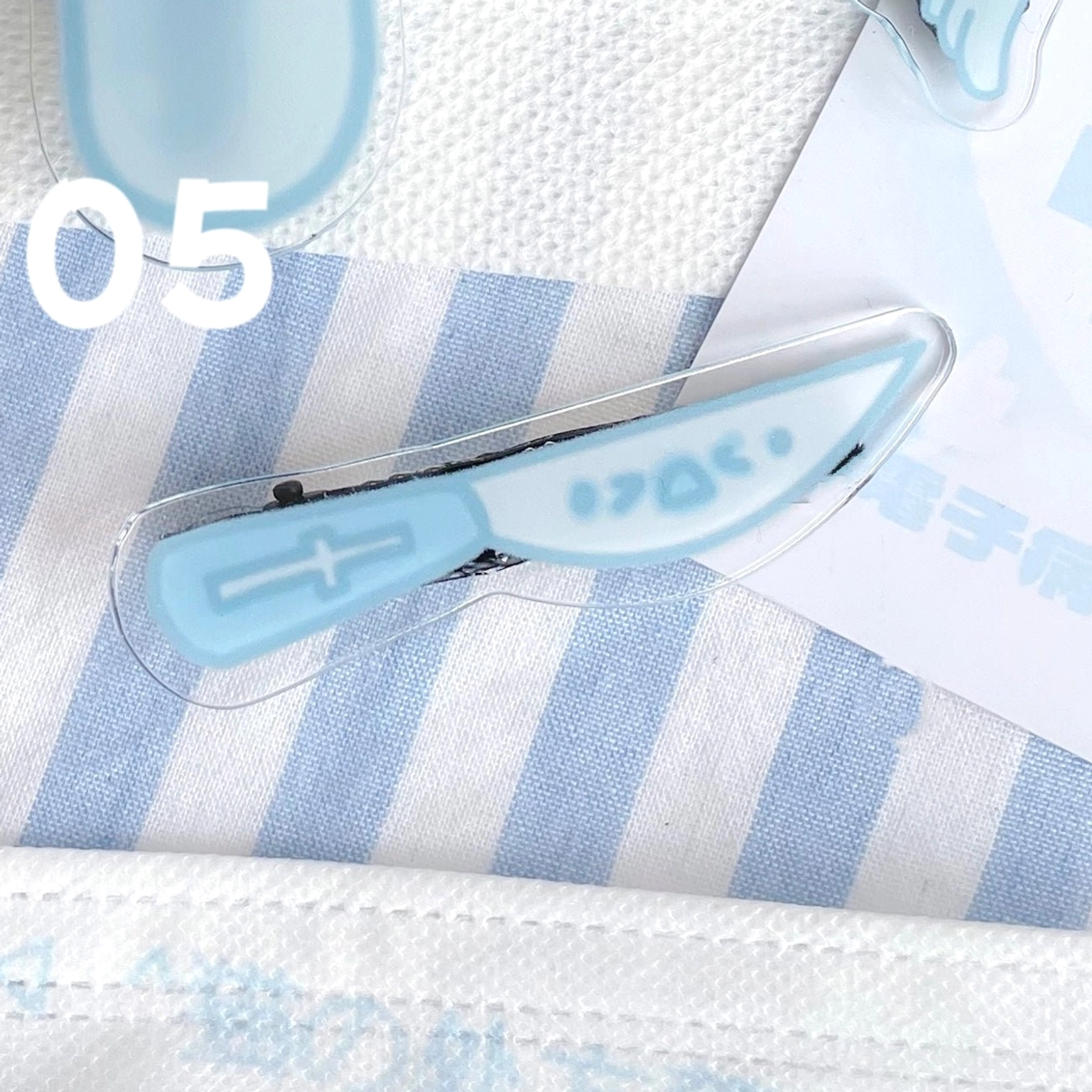Knife shaped Tenshi Kaiwai acrylic hair clip with cross patterns and text design light blue blade style on blue-striped fabric