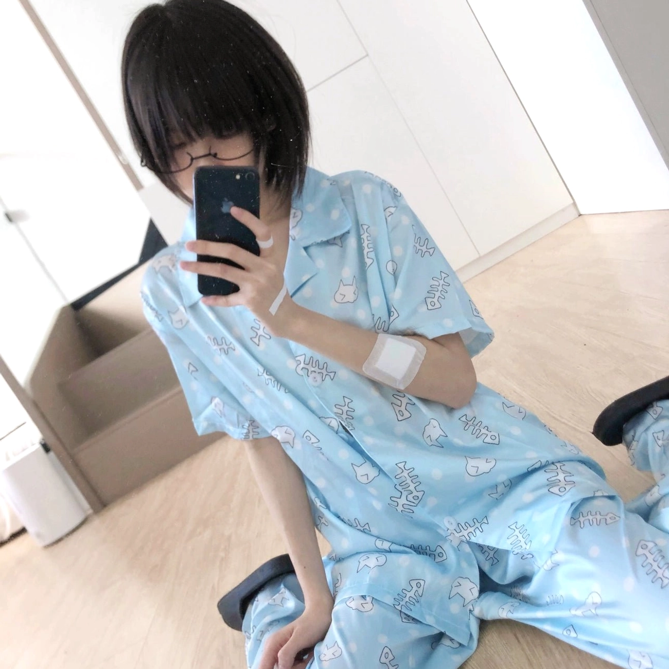 Female model wearing light blue Tenshi Kaiwai cat print short-sleeve pajama set, front selfie view in home bedroom with wooden floor aesthetic