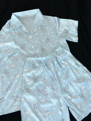 Tenshi Kaiwai light blue cat print short-sleeve pajama set with fishbone pattern, flat lay top view on black background showing satin texture detail