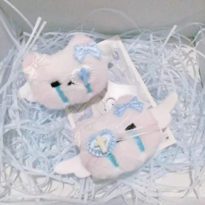 Plush crying kitty hair clip collection inside decorative gift box with light blue shredded packing and anime postcard showing mixed bow accents cross-heart patches and angel wings details