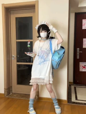 Tenshi Kaiwai anime print cotton long t-shirt with white lace hem, milky white base with blue-pink graphic, drop-shoulder oversized fit, full front view on masked model in residential entryway setting