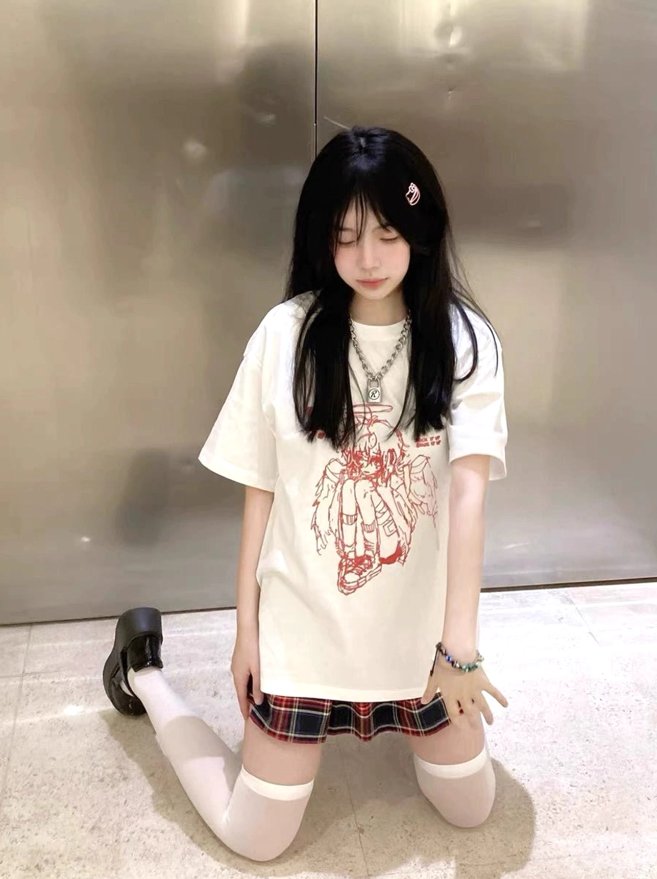 Female model wearing white Tenshi Kaiwai crying angel graphic t-shirt kneeling sideways angle metal wall plaid skirt white socks
