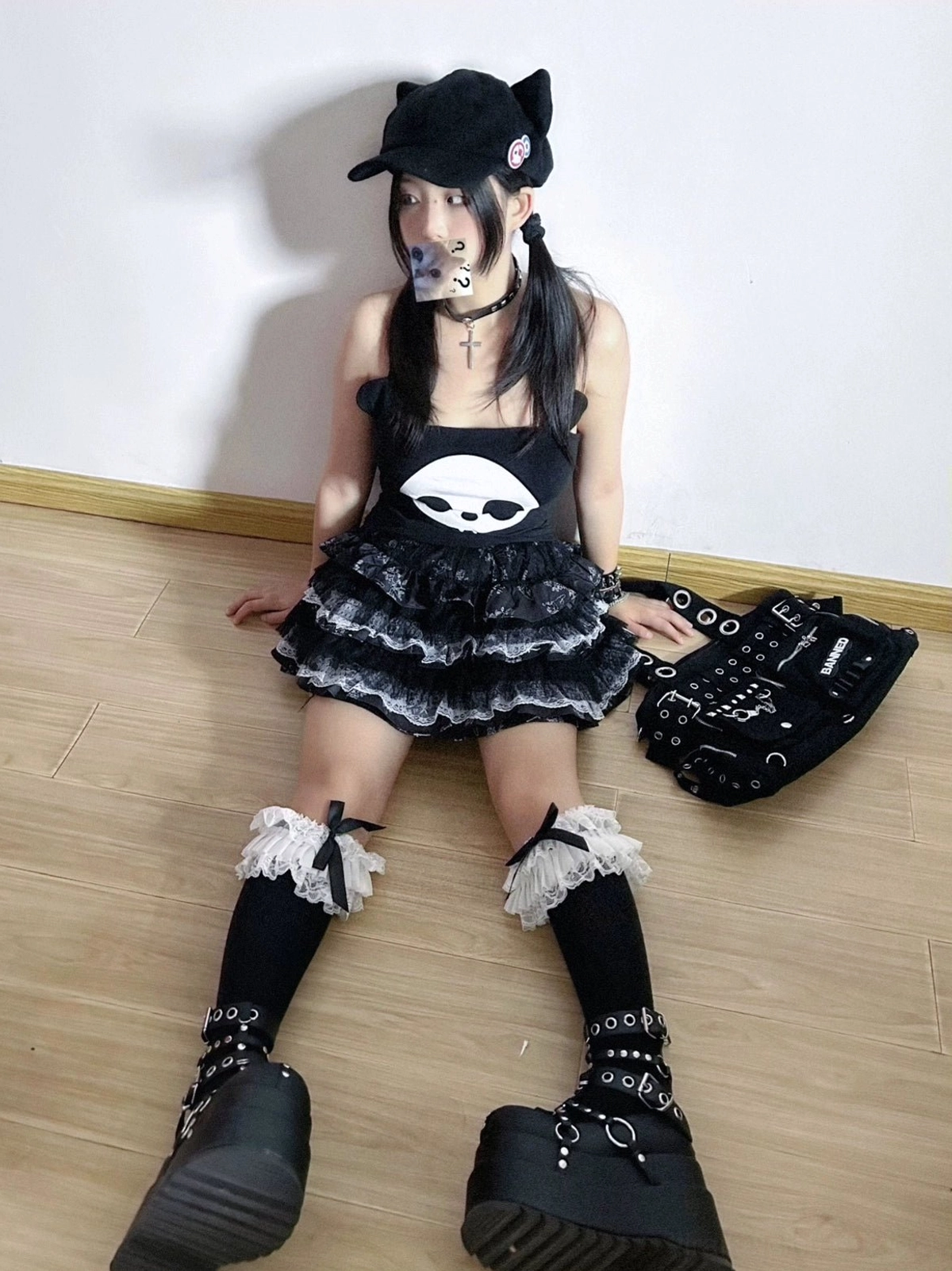 Seated full body shot of model in tiered ruffle lace puff skirt skull cami top ruffle leg cuffs cat ear baseball cap