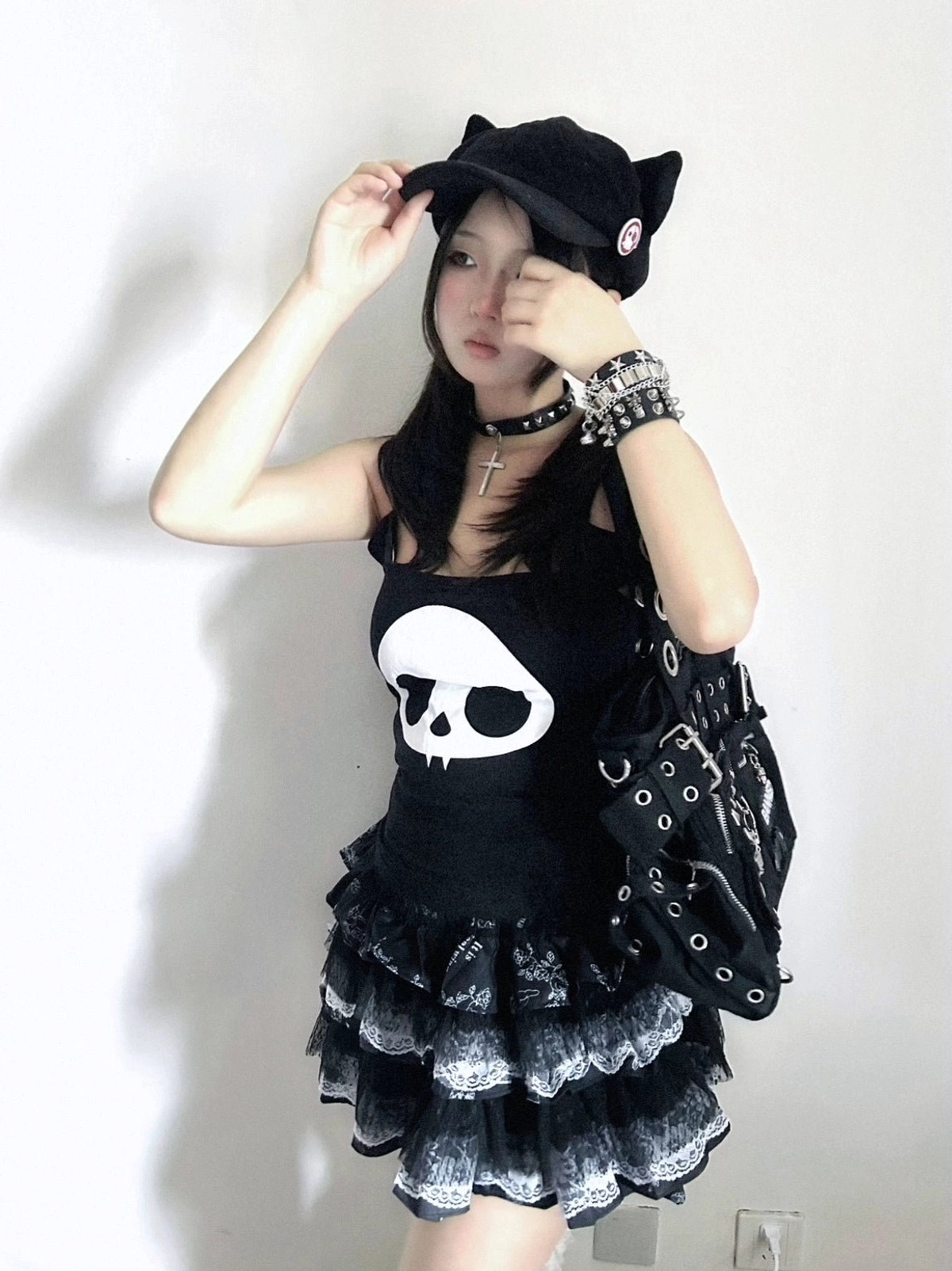 Three-quarter front portrait of girl adjusting cat ear baseball cap wearing tiered ruffle lace puff skirt skull print cami and studded bracelet