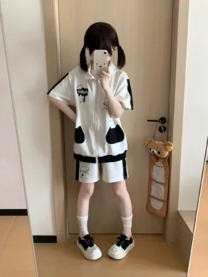 White and black angel kitten Jirai Kei two-piece set worn by twin-tailed model in mirror selfie, showcasing cute cat print zip-up sweatshirt and matching pocket shorts