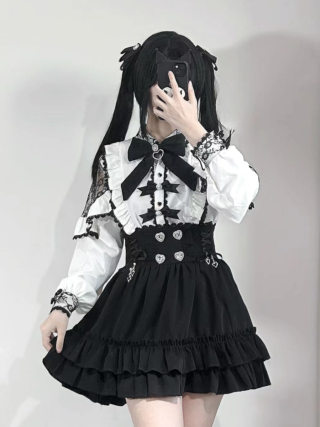 White Jirai Kei off-shoulder lace blouse with black bow tie and heart waist buttons, worn by twin-tailed model in studio mirror selfie, showcasing gothic lolita aesthetic