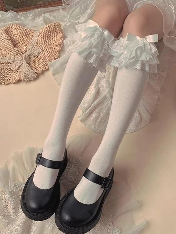 White Jirai Kei bow mid-calf socks with ruffled lace satin bow details knit material black Mary Jane shoes woven mat lace background overhead view