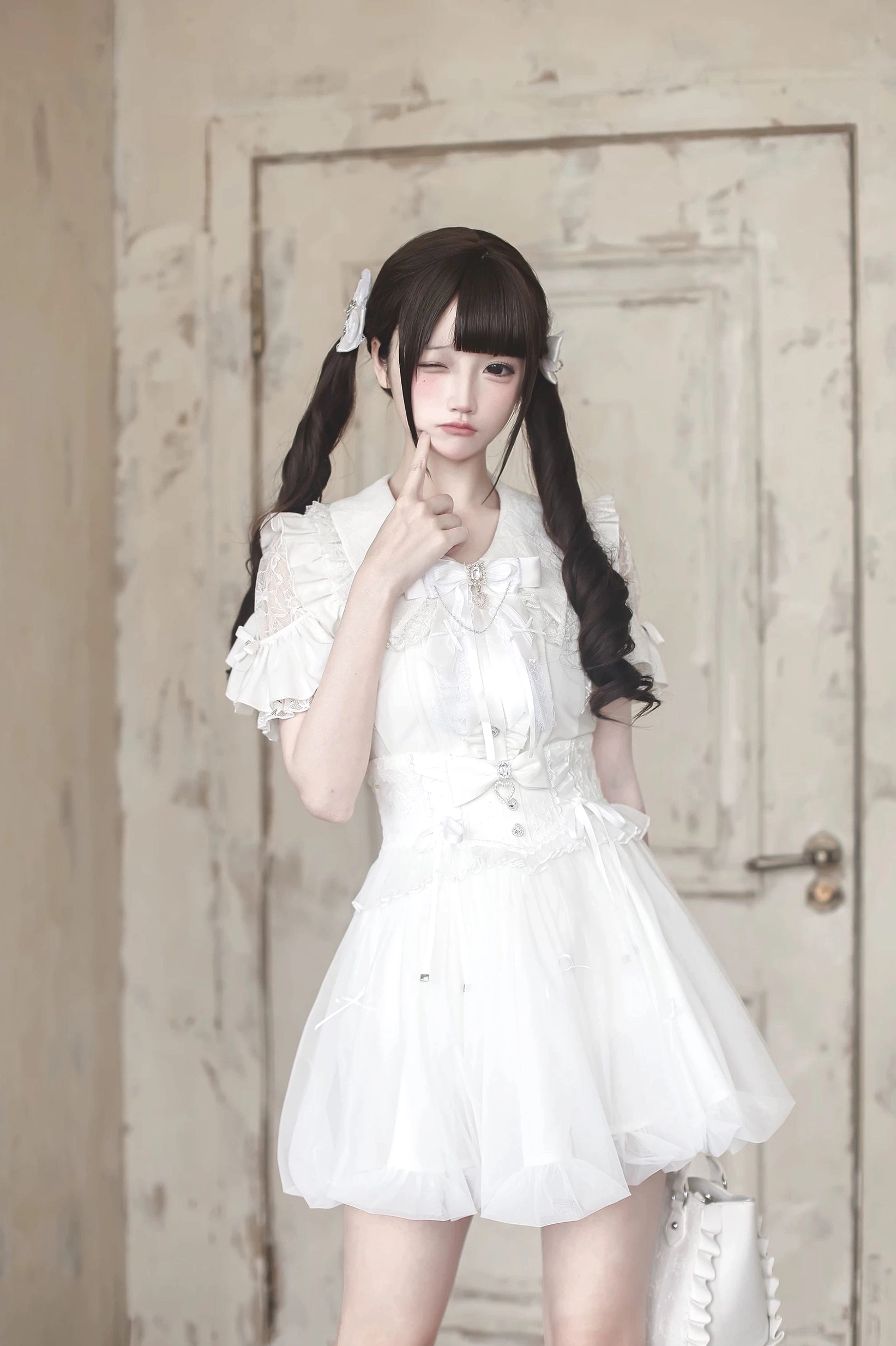 White Jirai Kei bubble dress with puff ruffled sleeves, rhinestone and bow details on tulle skirt, half-body shot of model with twin tails indoor backdrop