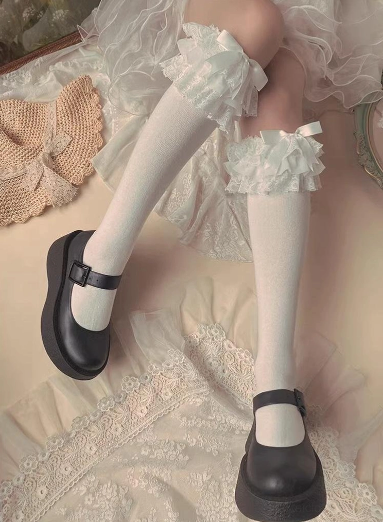 White Jirai Kei frilled bow socks with separate ruffled bow cuffs stretch fabric single leg black Mary Jane shoe lace backdrop side three-quarter view