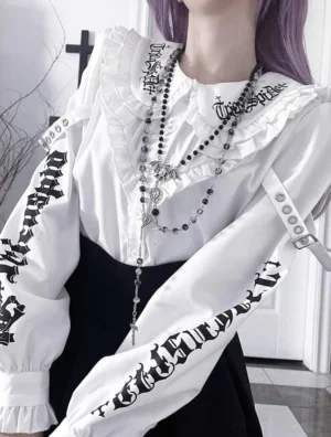 White Jirai Kei gothic blouse with skull prints and peter pan collar worn by model with purple hair in gothic indoor setting, front half-body close-up view