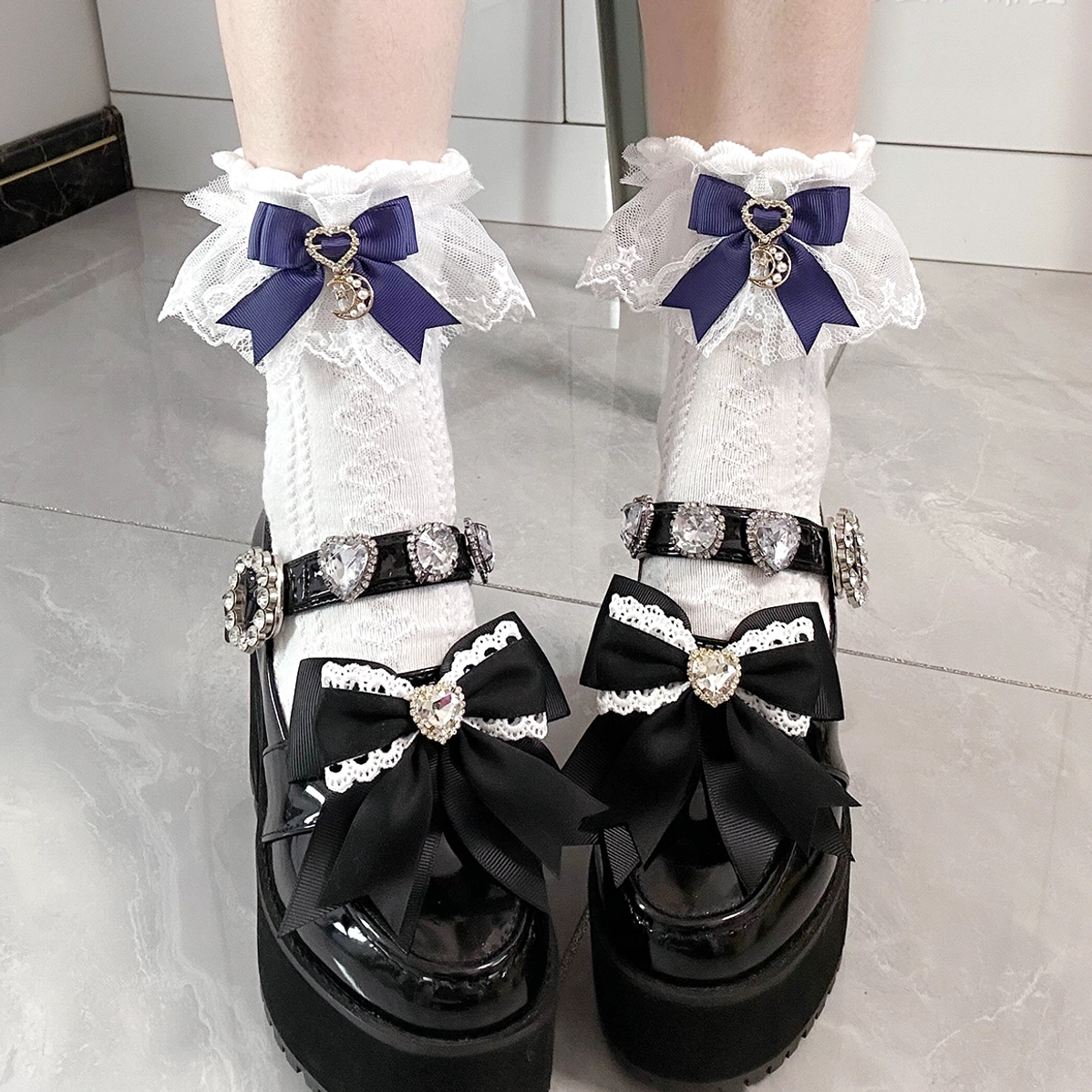 White Jirai Kei lace bow ankle socks with navy moon heart charm, styled with black platform Lolita shoes, close-up overhead view