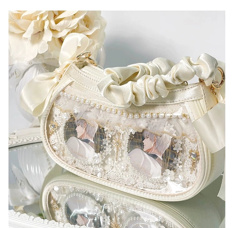White Jirai Kei mini ita bag with shimmery satin finish, clear dual badge display windows, and delicate lace trim with pearl accents, styled with artificial roses and mirrored tabletop for overhead front view