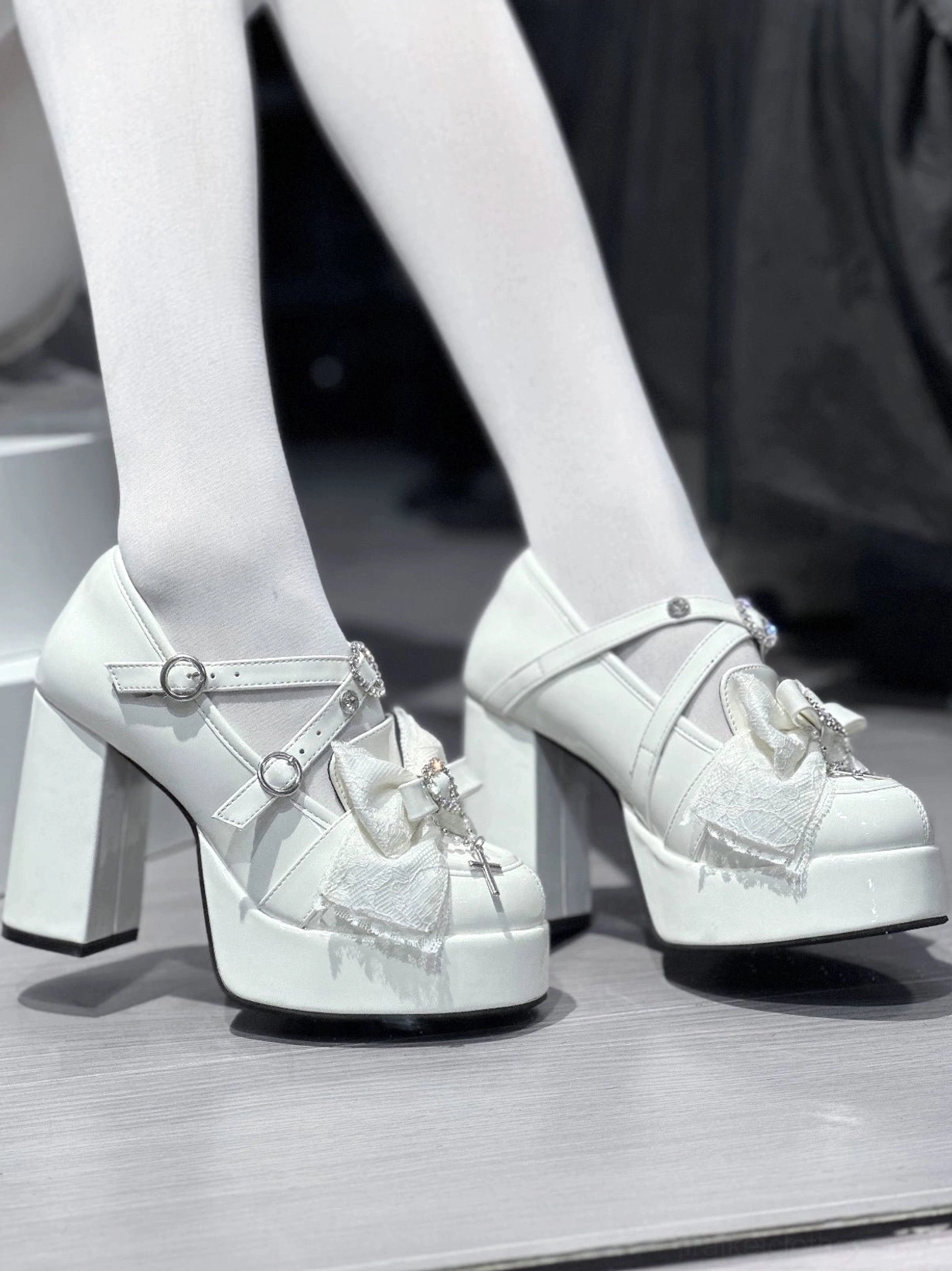 Side rear angle of white patent Jirai Kei platform heels showing chunky block heel structure, heart rhinestone cross pendant accent, and platform sole thickness