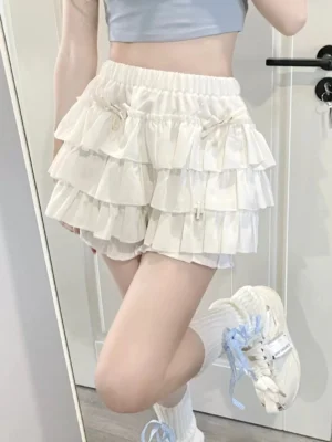White ruffle pumpkin shorts skirt with bow accents and elastic waistband styled with cropped top and sneakers, front mirror shot displaying tiered frills design