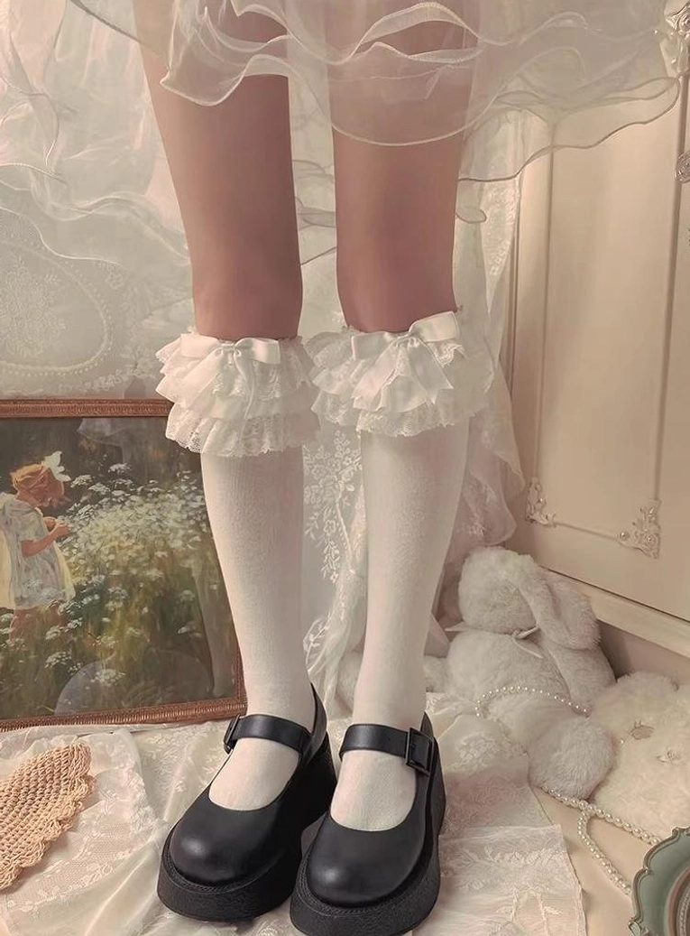 White Jirai Kei ruffled lace mid-calf socks with double-layer frills worn with black Mary Jane shoes against vintage indoor decor backdrop straight front view
