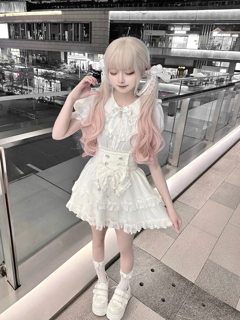 White lolita two-piece set close-up three-quarter view with model wearing hair bows, head-down pose emphasizing ruffled dress hem, delicate lace details, and suspender construction