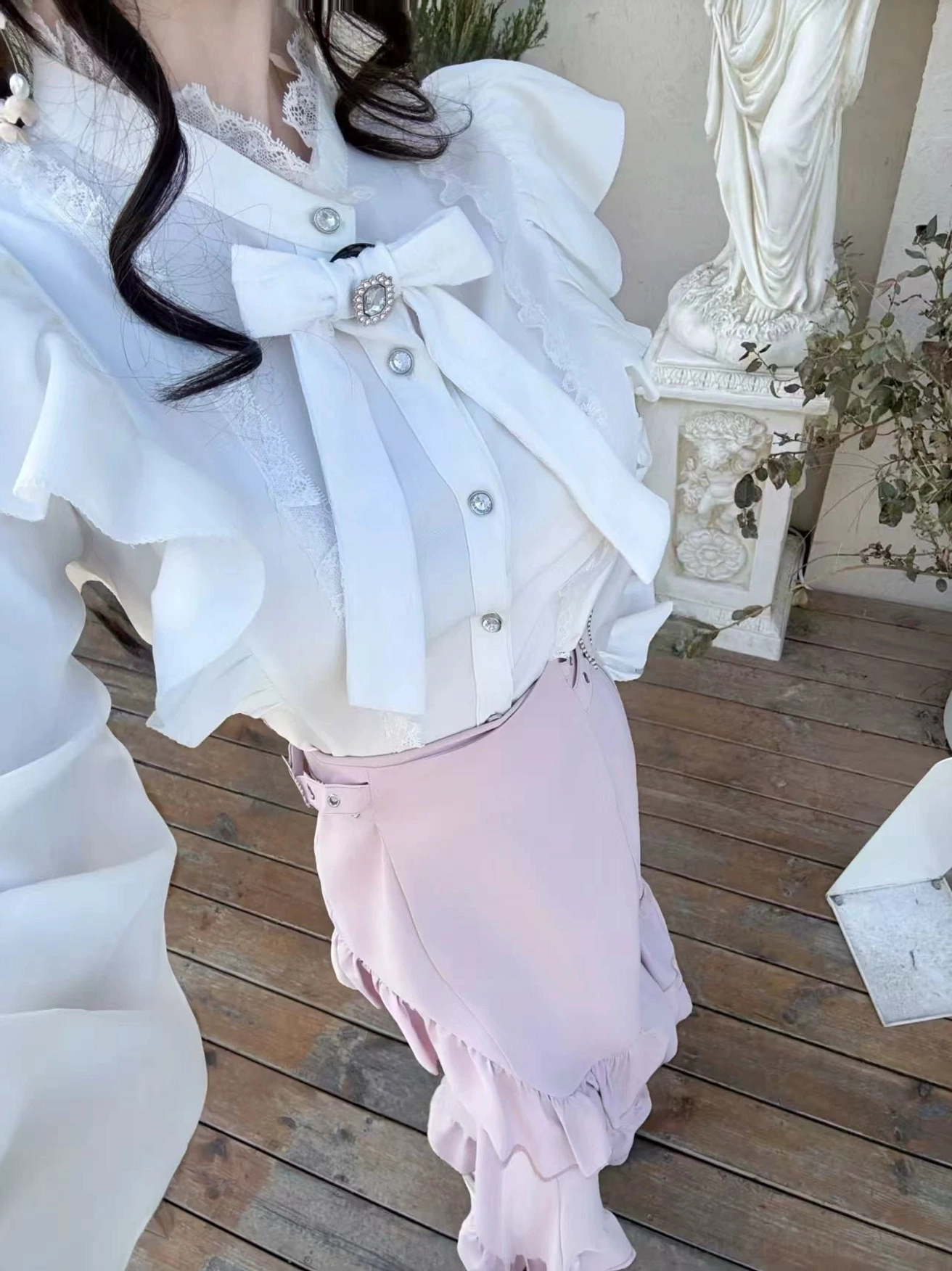Close-up front three-quarter view of white blouse featuring lace-trimmed collar, crystal-embellished round diamond buttons, and pink fishtail skirt with metal waist buckle detail