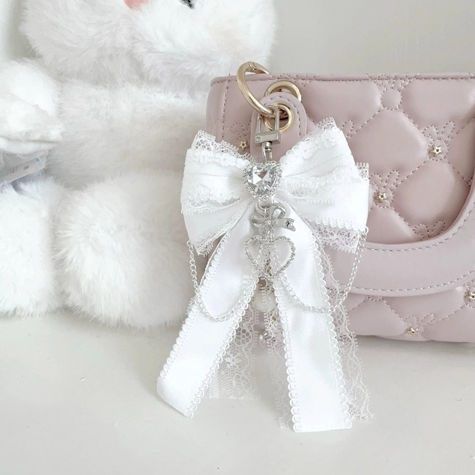White Ryousangata bow bag pendant with heart rhinestone and multi-chain charm on quilted handbag - close-up eye-level view of delicate lace bow and sparkle detail