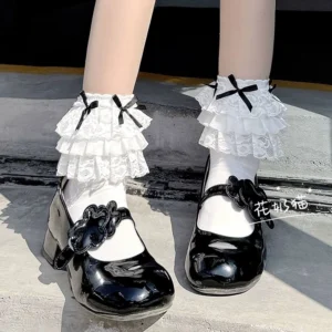 White lace bow mid-calf Jirai Kei socks with triple-layer ruffle cuff and black bow accents, styled with black patent leather Mary Jane shoes, close-up front view showcasing lace detail